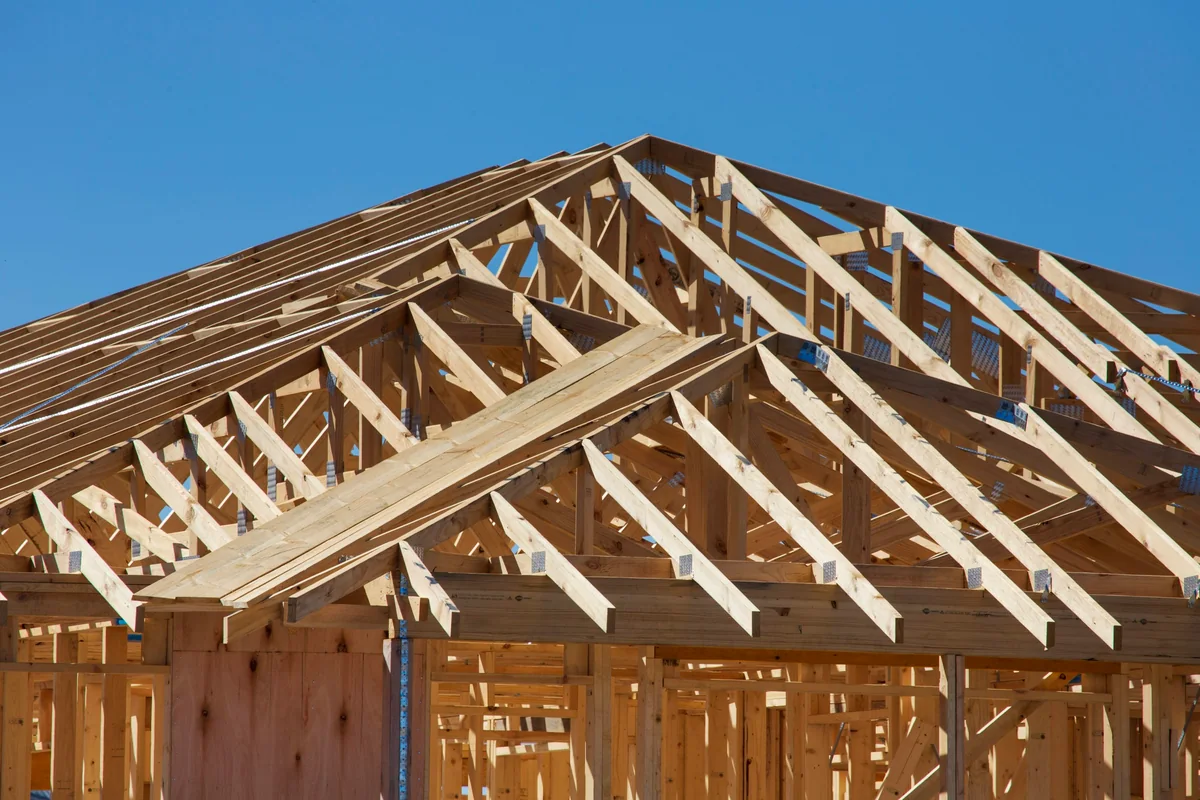 Chantier d'une maison à ossature bois : murs à montants et fermettes de charpente en bois clair sous un ciel bleu