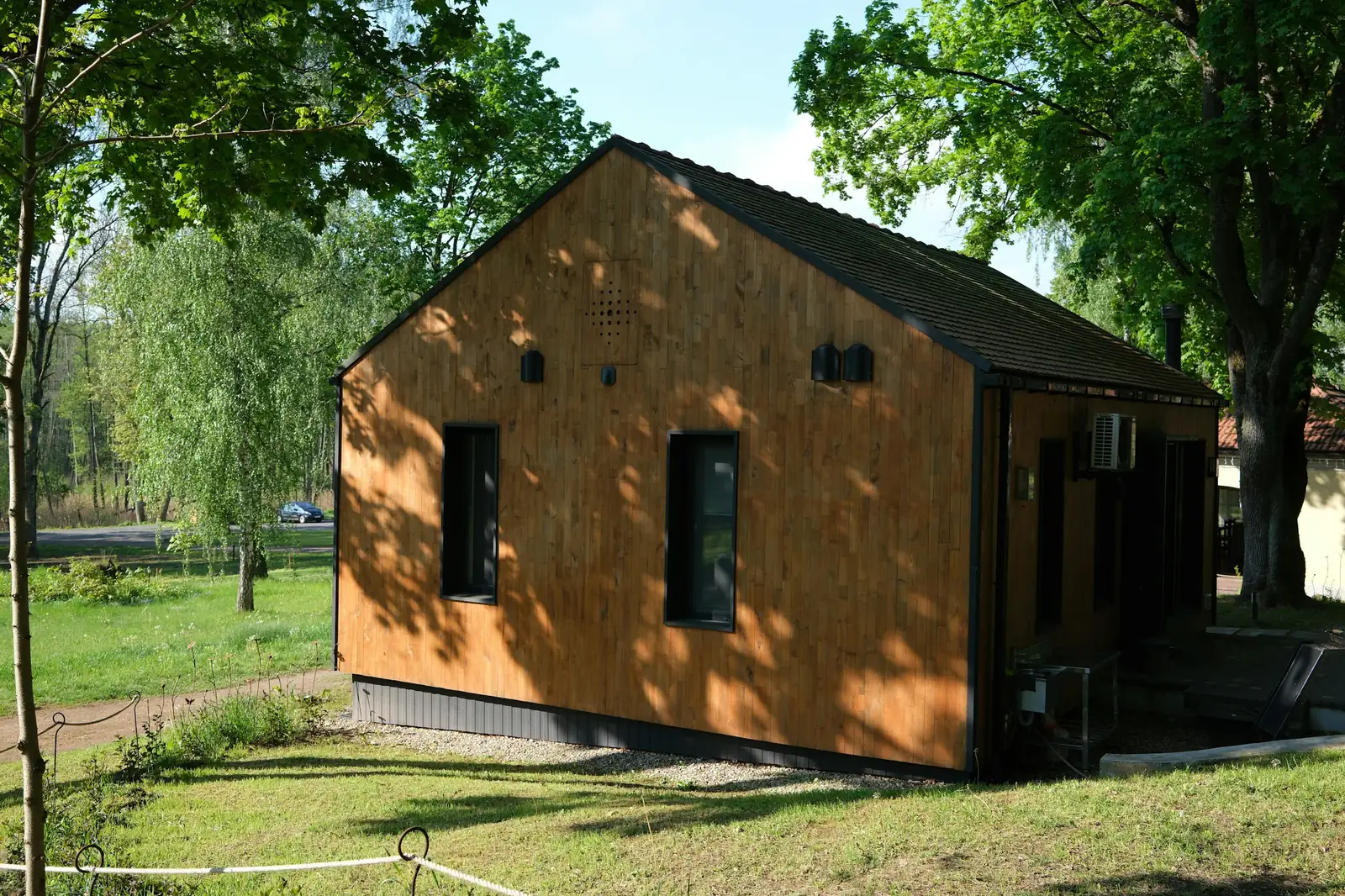 Maison de plain-pied à bardage bois vertical et toit à deux pans, posée sur une pelouse à l'ombre de grands arbres