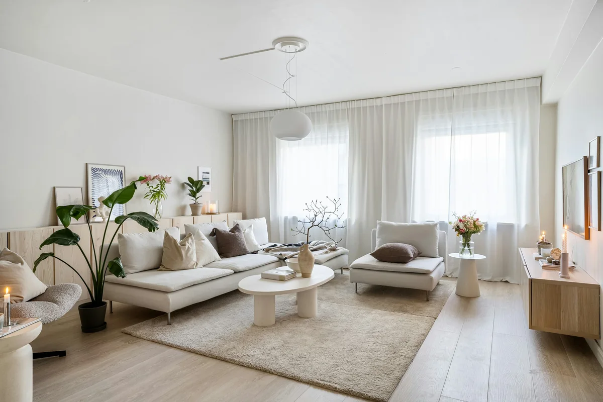 Séjour lumineux aux murs et au plafond blancs, avec un canapé clair, un tapis beige et un parquet clair