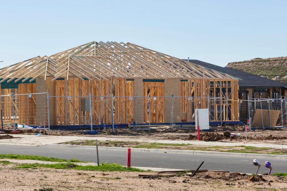 Maison de plain-pied en construction : murs à ossature bois et charpente en fermettes derrière une clôture de chantier