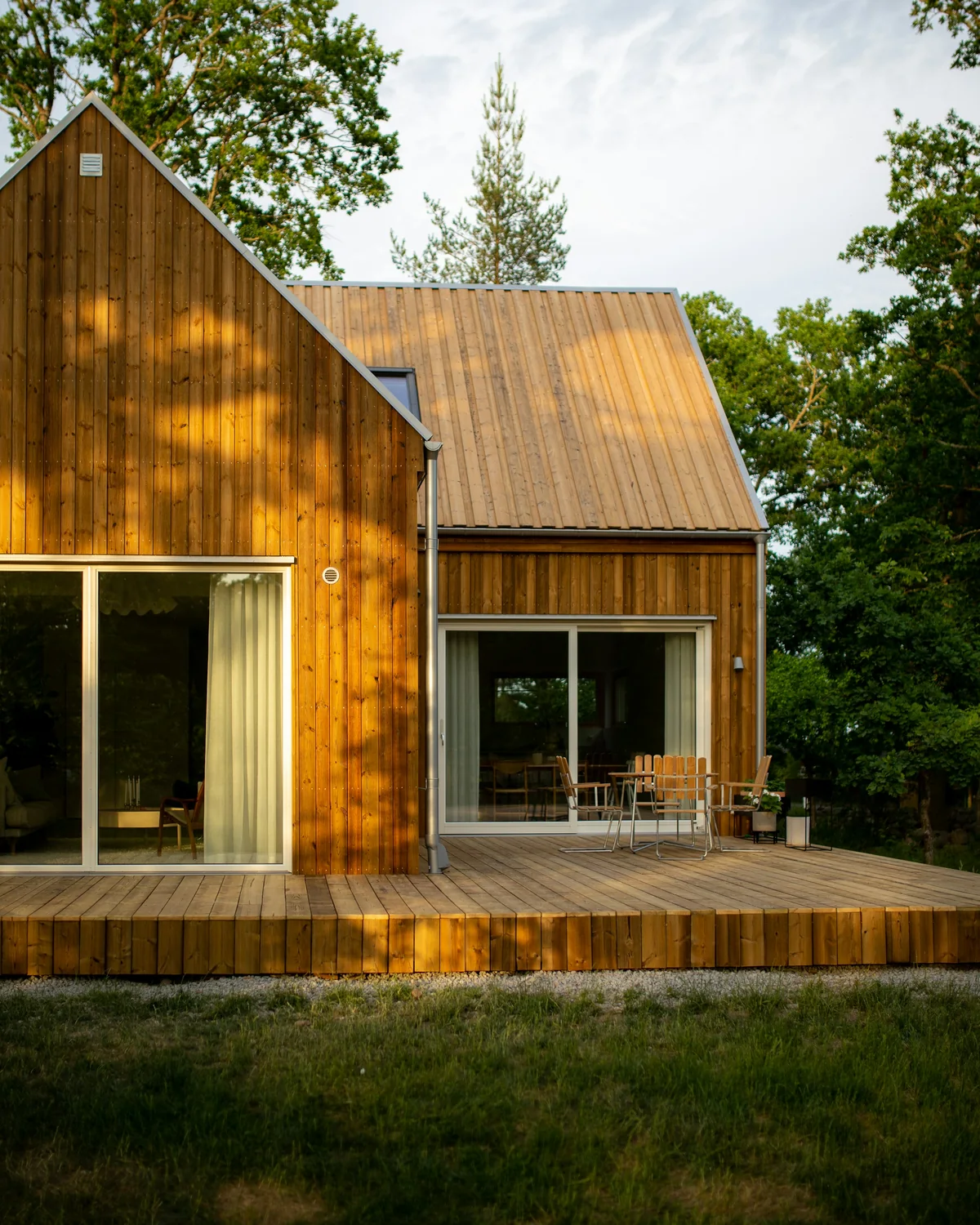 Maison à bardage bois vertical avec deux baies vitrées donnant sur une terrasse en bois meublée, dans un jardin
