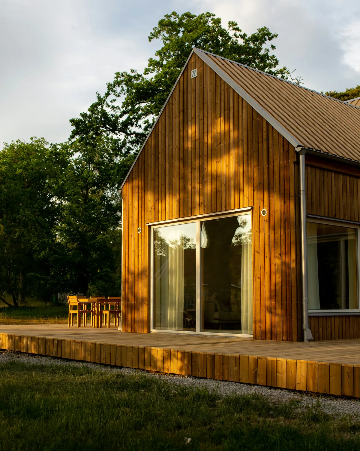Pignon d'une maison à bardage bois vertical avec une baie vitrée, ouvrant sur une terrasse en bois avec table et chaises